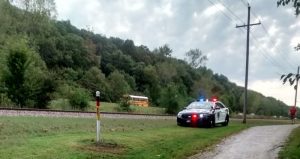 Police car with flashing lights next to railroad in English Landing Park with school bus behind