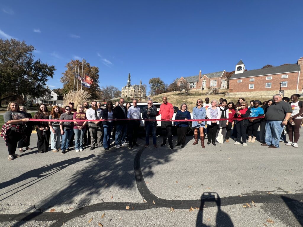 A group of people standing behind a ribbon, waiting for it to be cut